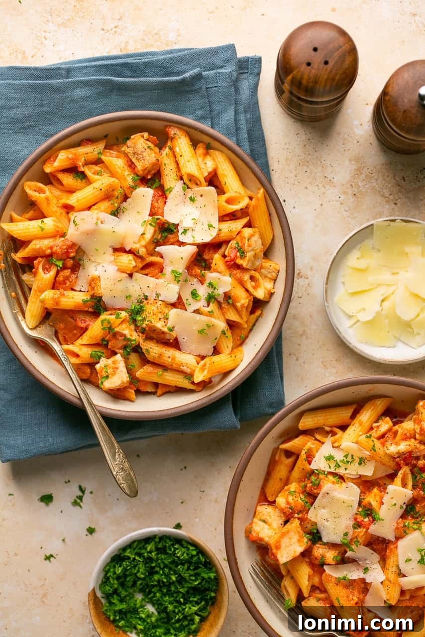 Chicken and penne vodka in bowls on top of a blue towel with fresh parmesan on the side