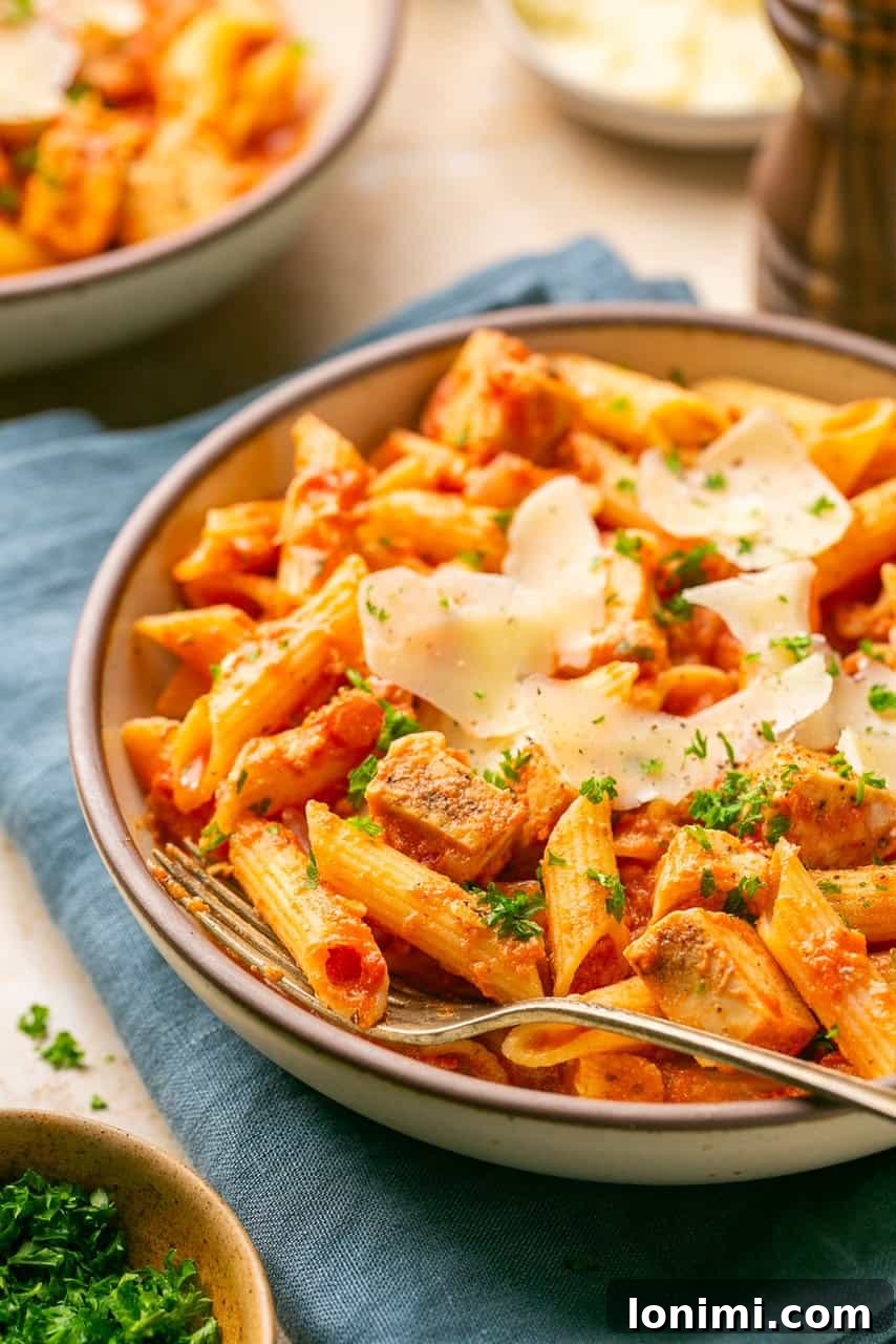 A side view of a bowl of chicken and penne vodka topped with parsley