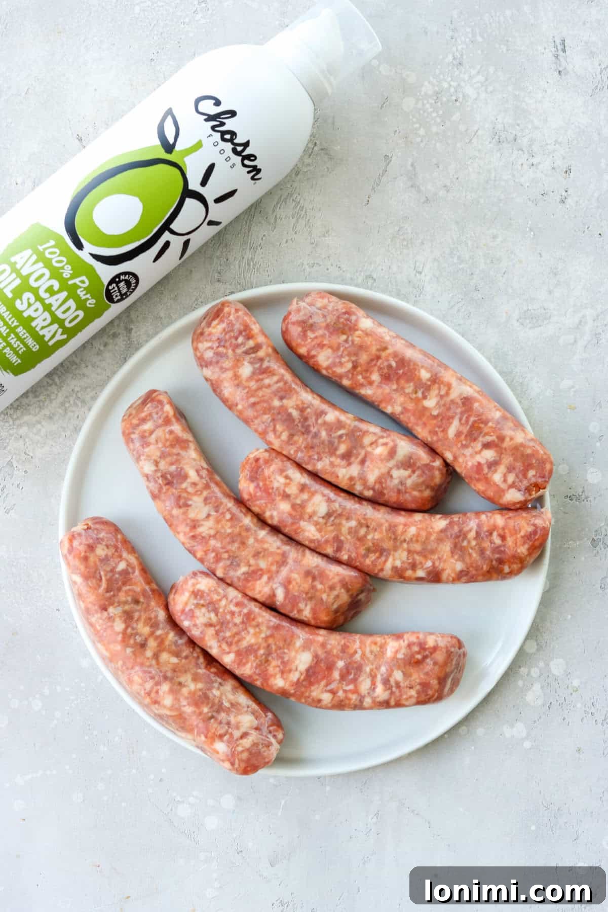 Raw Italian sausages and a bottle of avocado oil on a wooden cutting board.