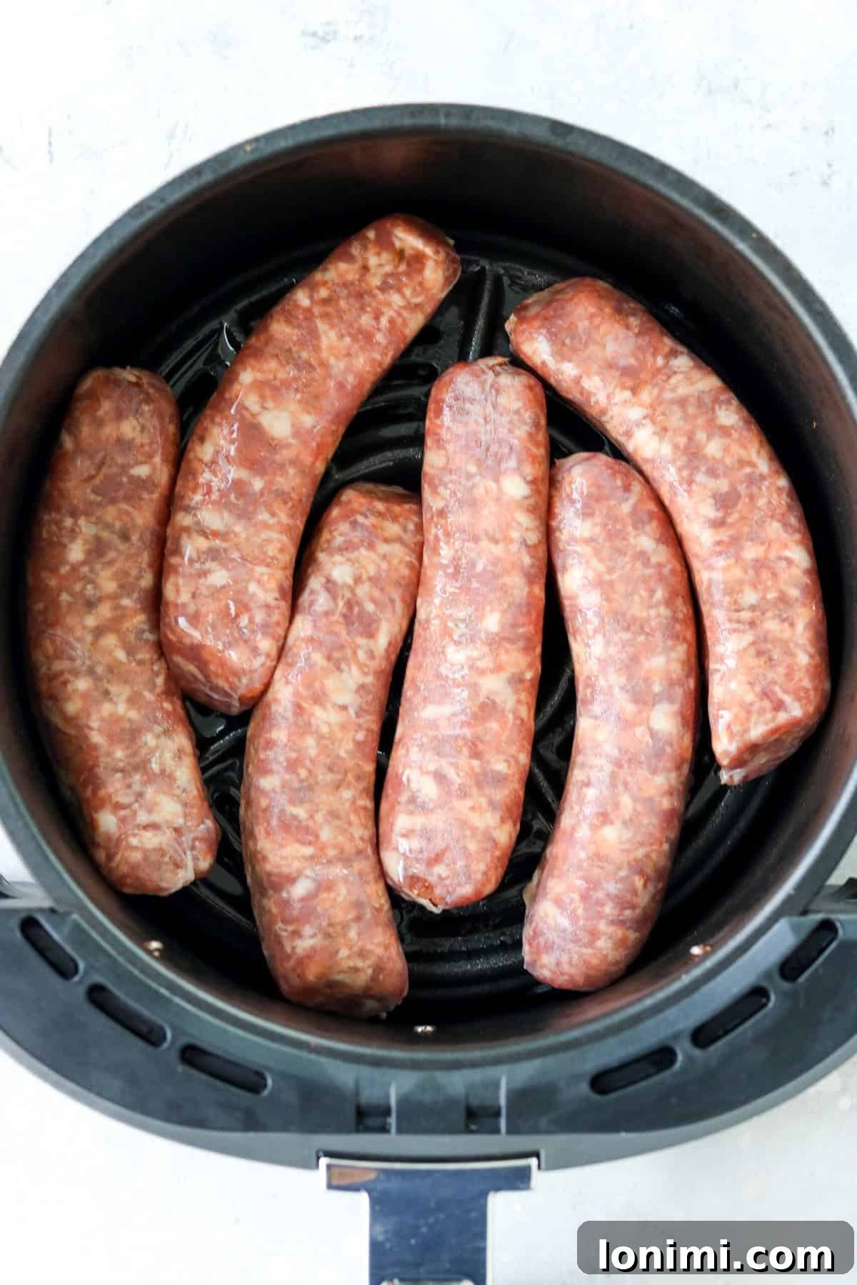 Raw Italian sausages arranged neatly in a single layer within an air fryer basket.