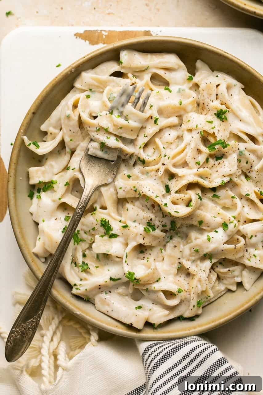 tagliatelle pasta with alfredo sauce in a bowl with a fork topped with parsley