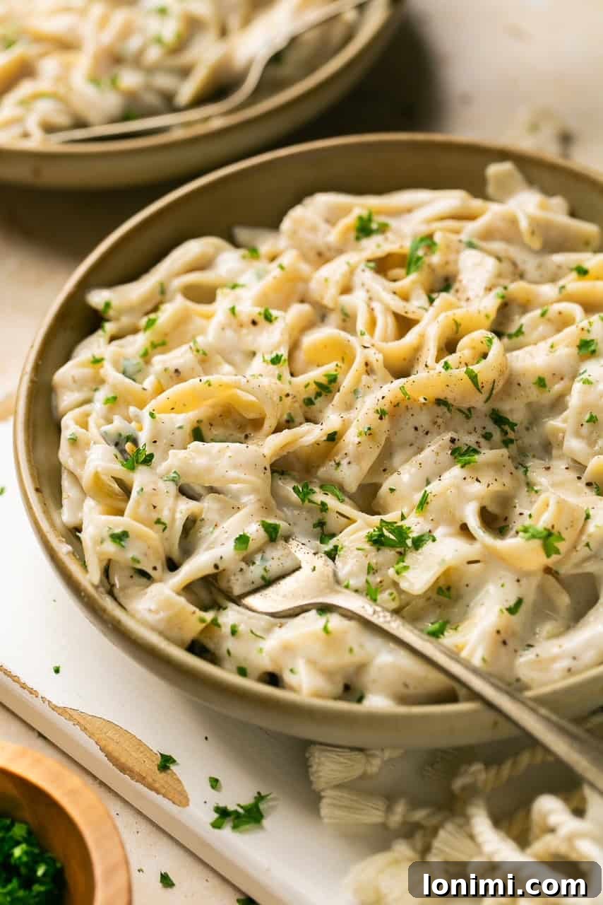a bowl of pasta with alfredo sauce topped with parsley with a fork in it