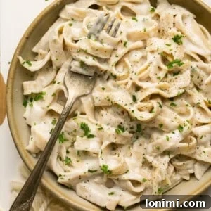 tagliatelle pasta with alfredo sauce in a bowl with a fork topped with parsley