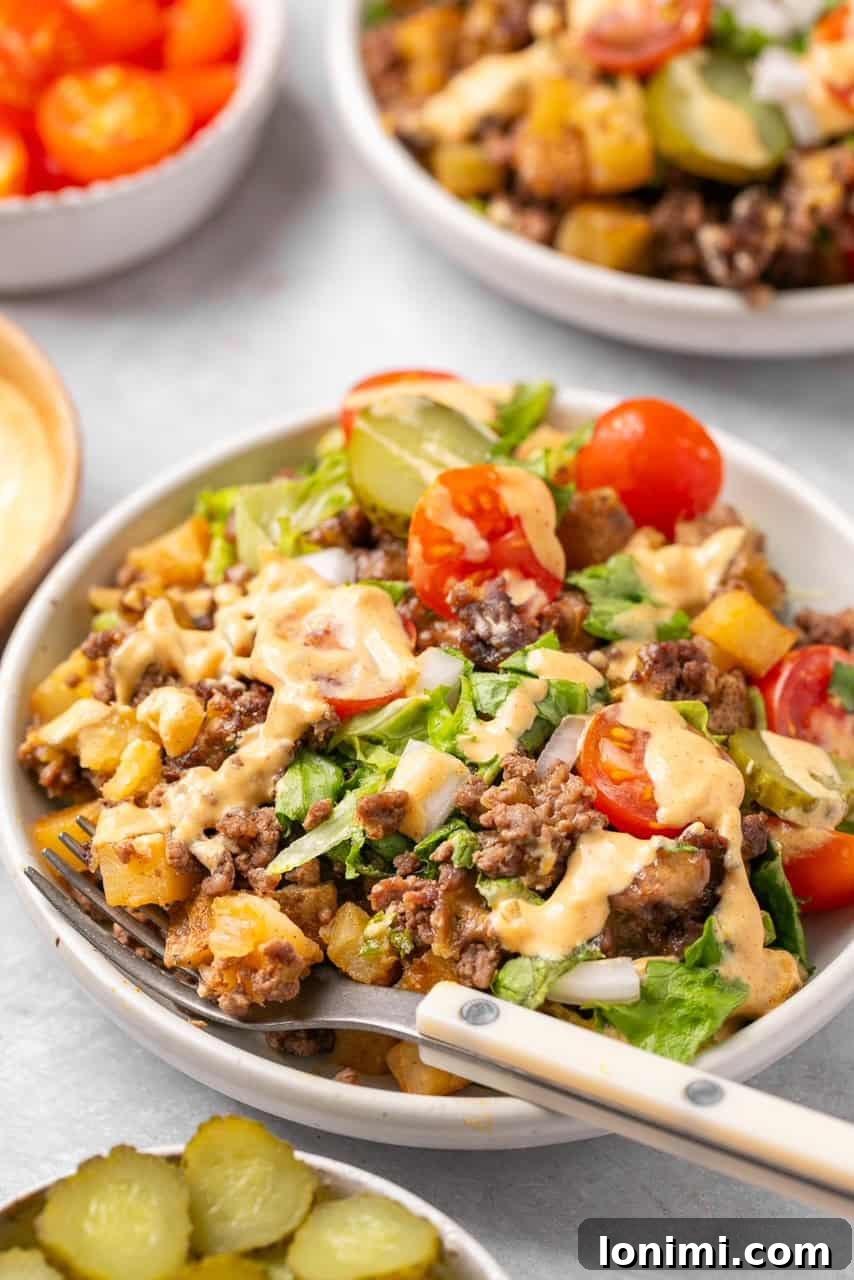 A delectable bowl of Big Mac Casserole, garnished with fresh lettuce, tomatoes, and a wooden fork ready to dig in.