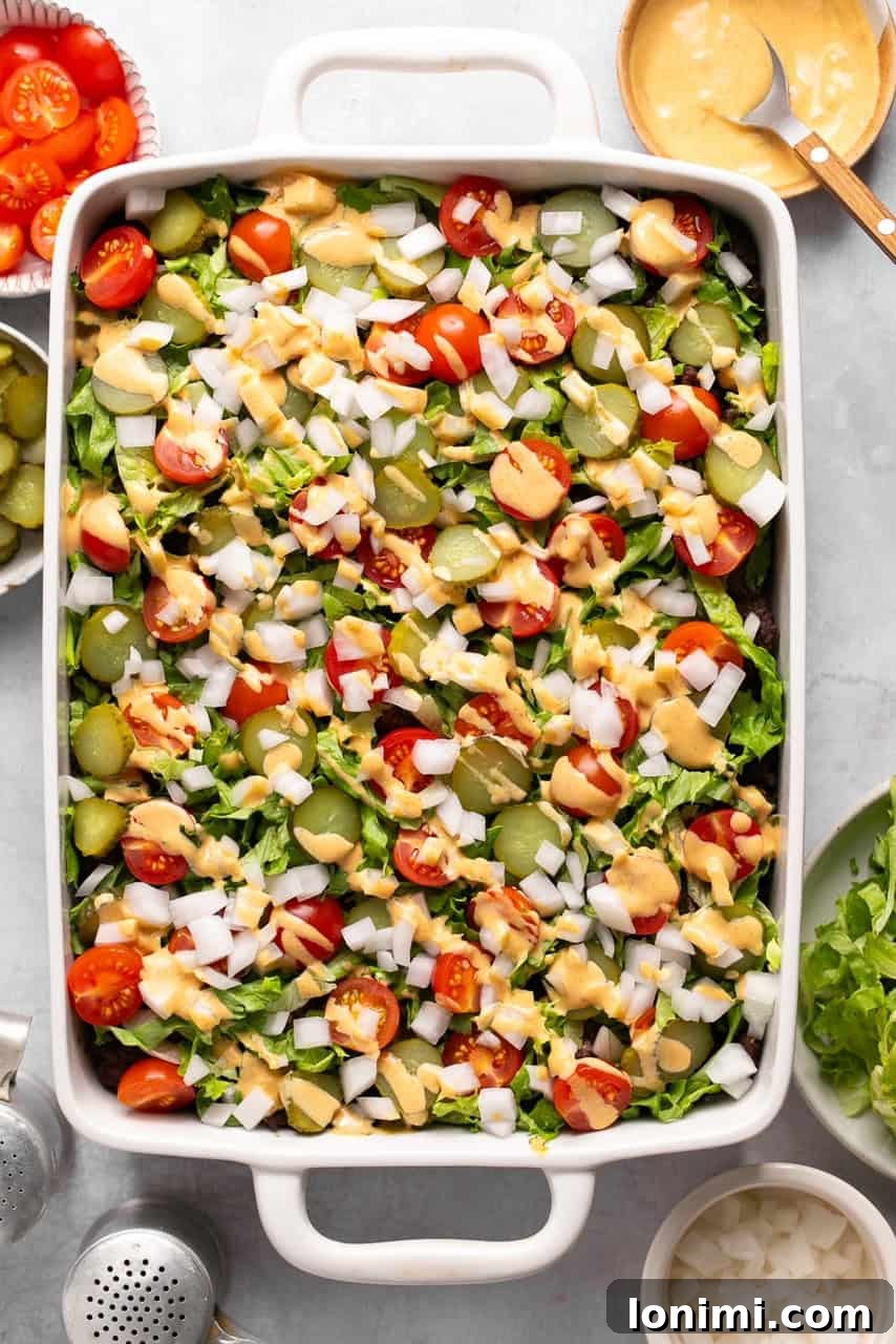 A close-up shot of the finished Big Mac Casserole, showcasing layers of potatoes, ground beef, melted cheese, and fresh toppings drizzled with special sauce.