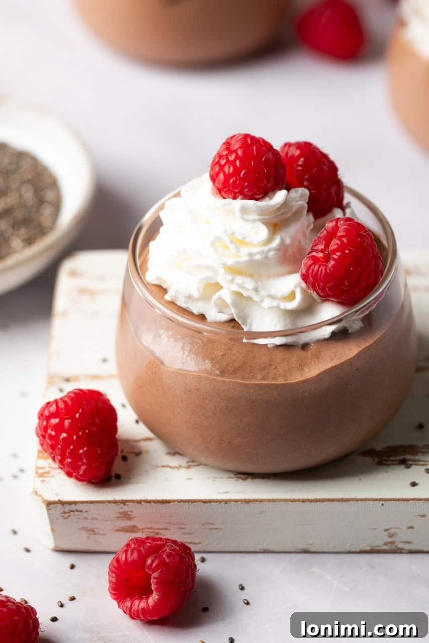 Chocolate protein chia seed pudding in a glass jar topped with luscious whipped cream and fresh vibrant berries.