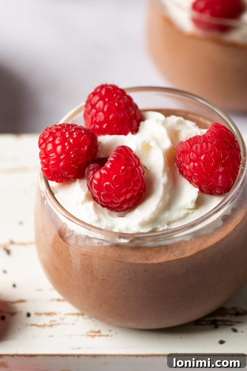 Close-up of a jar of freshly blended protein chia pudding with whipped cream and raspberries on top.