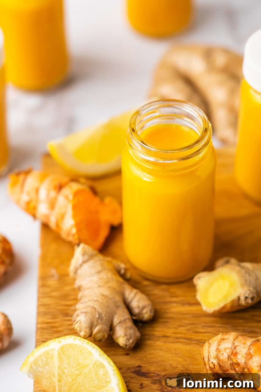 Lemon ginger turmeric shot in a small glass jar on a wooden cutting board with fresh ginger around it.
