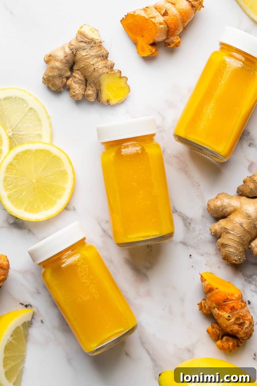Lemon ginger turmeric shots with white screw-on lids laying next to lemon slices, ginger, and turmeric