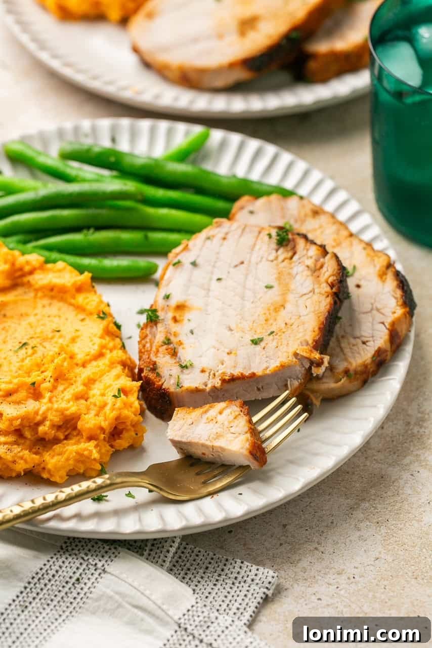 2 slices of pork roast on a plate with mashed sweet potatoes and green beans