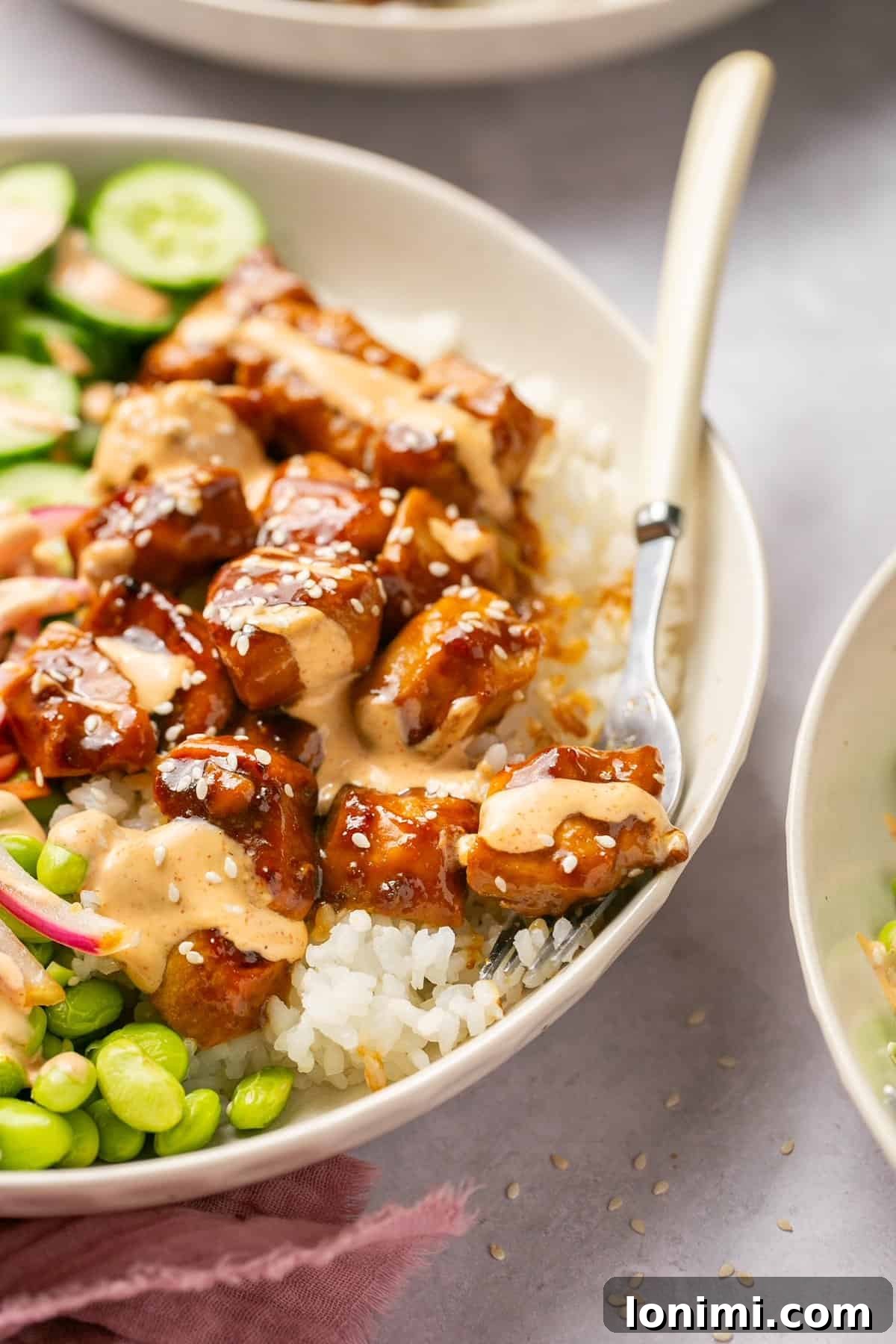 Effortless Teriyaki Chicken Poke Bowls with Fiery Sriracha Mayo 8 A fork taking a bite of chicken out of a bowl