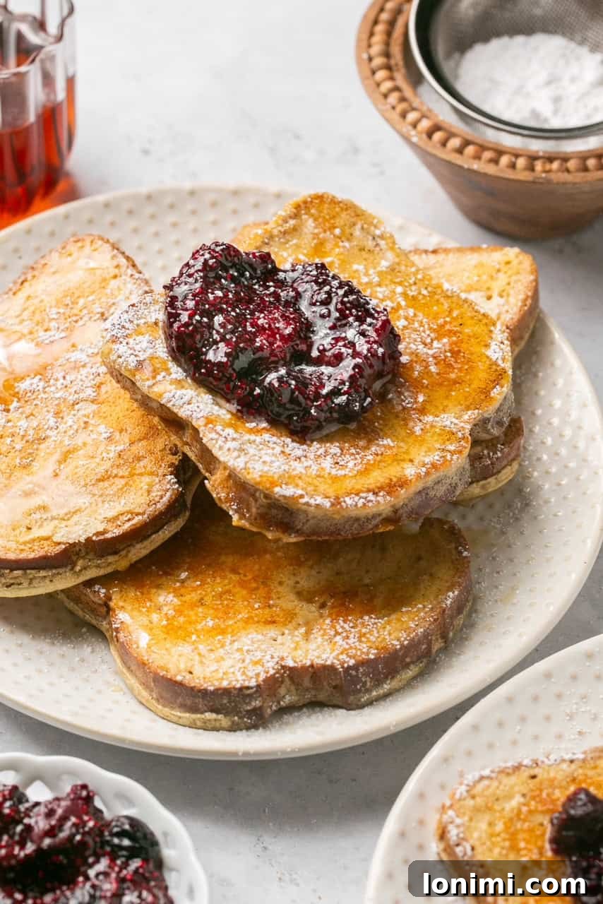 Four slices of golden brown protein french toast stacked on a plate, garnished with fresh berries and chia jam