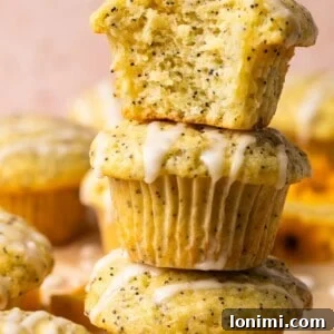 A stack of lemon poppyseed muffins with a bite taken out of one, showcasing their perfect texture and glaze.
