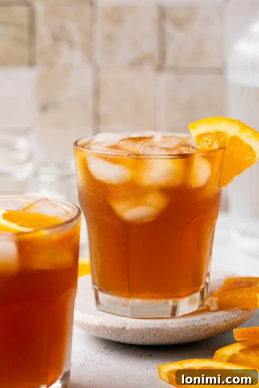 A vibrant Espresso Tonic in a glass, filled with ice cubes and garnished with a fresh orange wedge, ready for a refreshing sip.