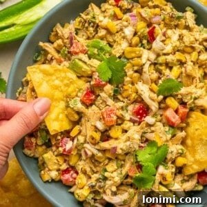 Mexican street corn chicken salad in a bowl with a hand holding a chip scooping out a bite, highlighting its texture and creaminess