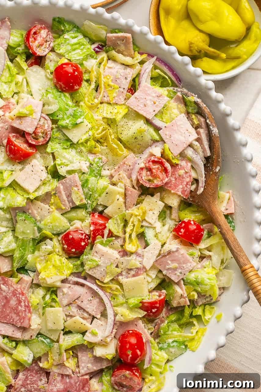 A vibrant Chopped Italian Grinder Salad in a white bowl, ready to be enjoyed with a wooden serving spoon.