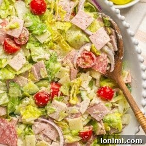 Italian grinder salad in a white bowl with a wooden spoon