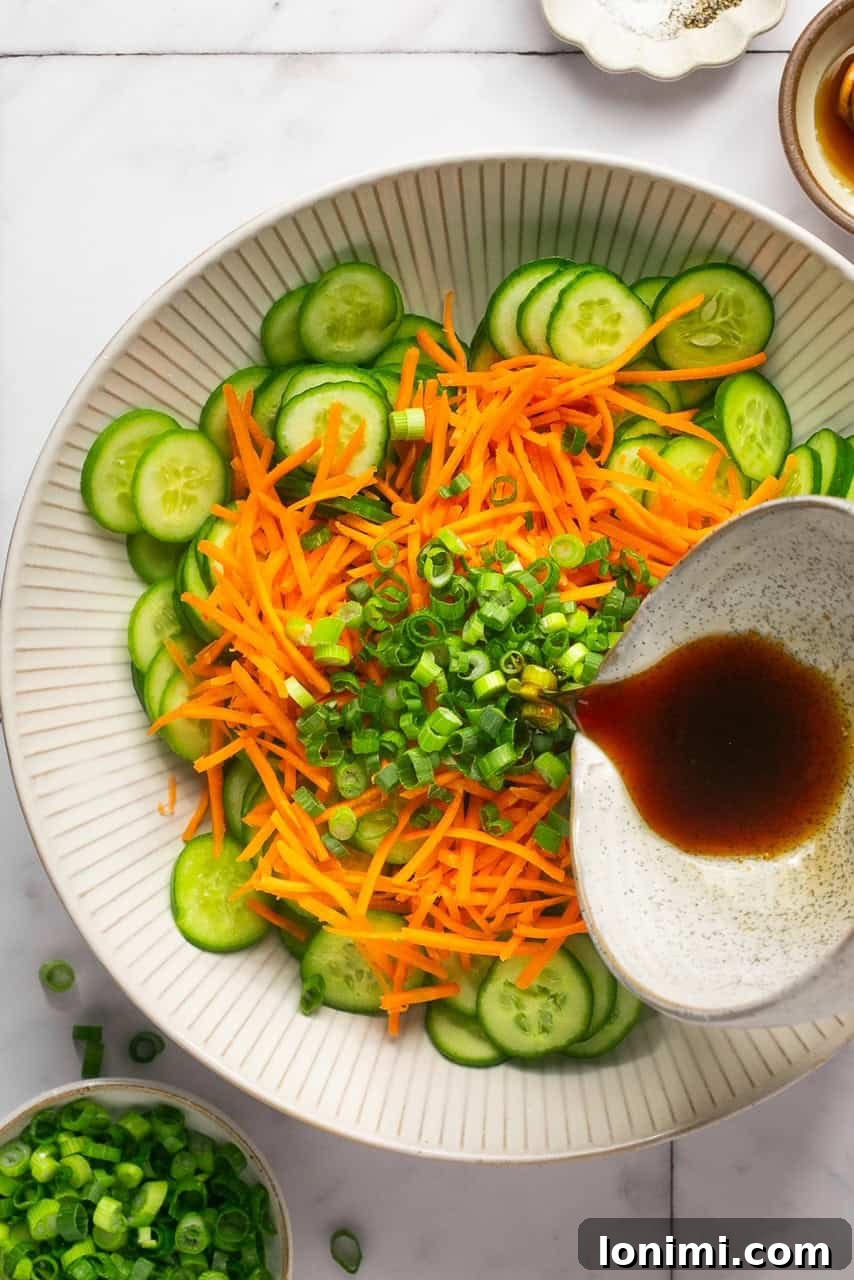 pouring dressing on top of a cucumber carrot salad