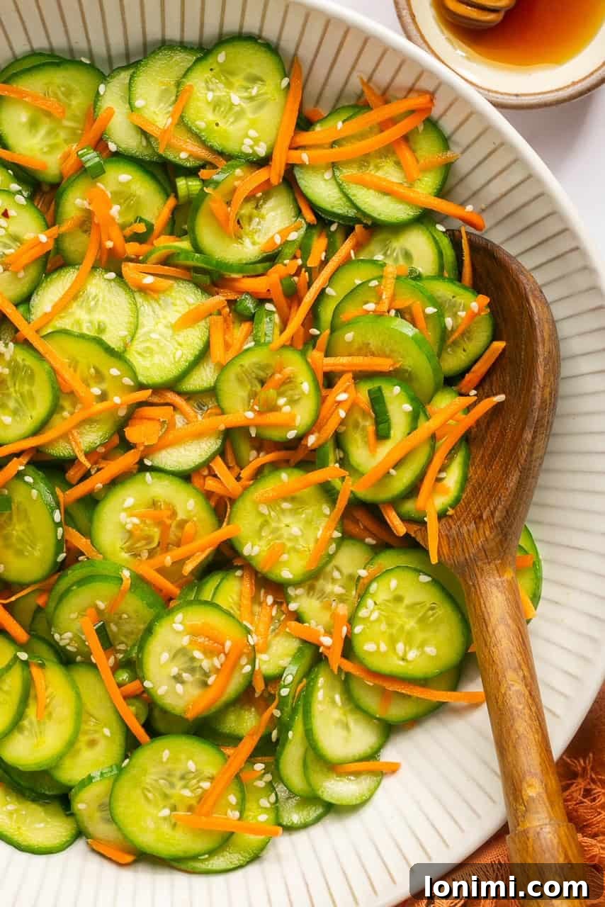 a close up view of a cucumber salad in a large bowl with a wooden spoon