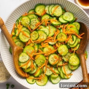 cucumber carrot salad with 2 wooden spoons in a white bowl