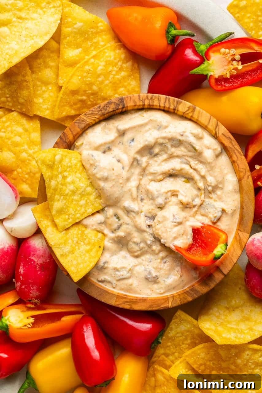 The Viral Protein-Packed Cottage Cheese Queso 2 Creamy cottage cheese queso in a rustic wooden bowl, artfully surrounded by crispy tortilla chips and fresh peppers, with a chip dipped invitingly into the center.