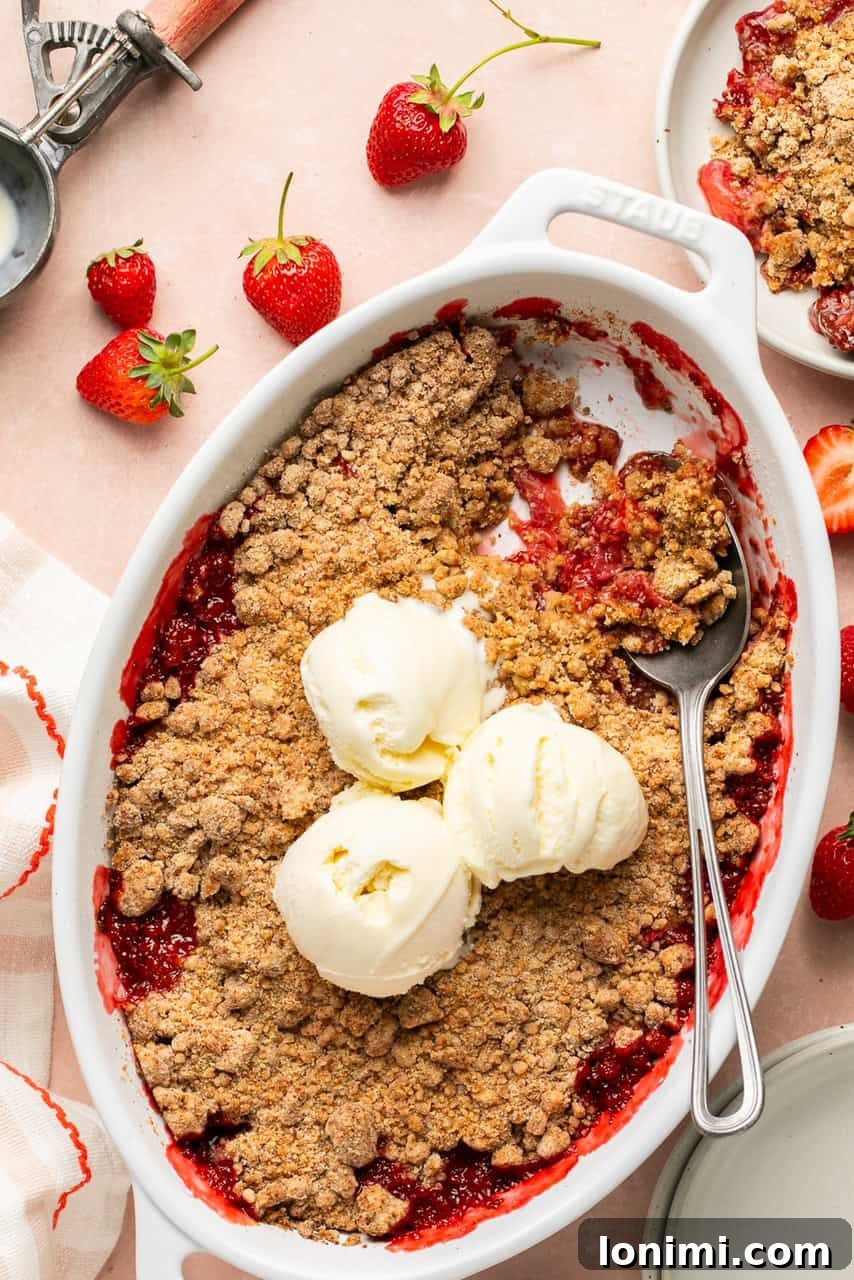 Pratik Glutensiz Çilekli Crumble 2 strawberry crumble in an oval baking dish topped with 3 scoops of vanilla ice cream with a spoon taking a portion out