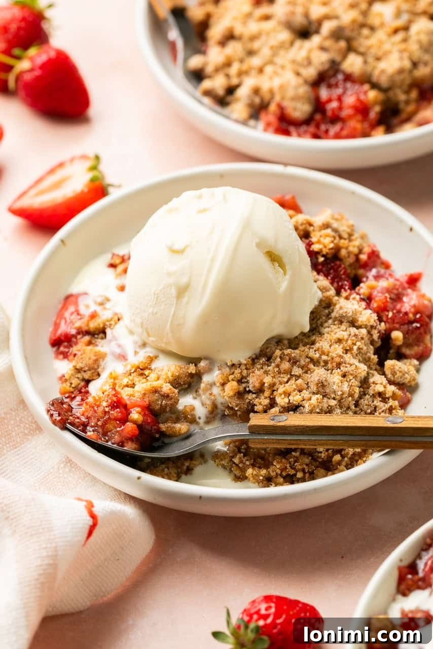 Pratik Glutensiz Çilekli Crumble 3 a slice of fruit crumble on a white plate with a scoop of vanilla ice cream