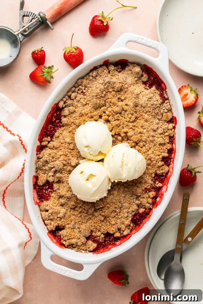 Pratik Glutensiz Çilekli Crumble 7 overhead shot of a strawberry crumble in a white baking dish topped with three scoops of vanilla ice cream