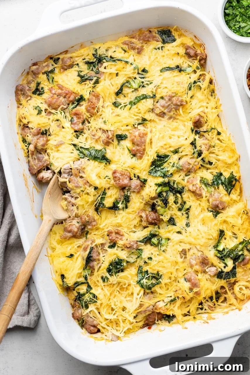 A large white baking dish filled with the creamy Tuscan Spaghetti Squash Casserole, with a serving spoon resting in it, ready to be dished out.