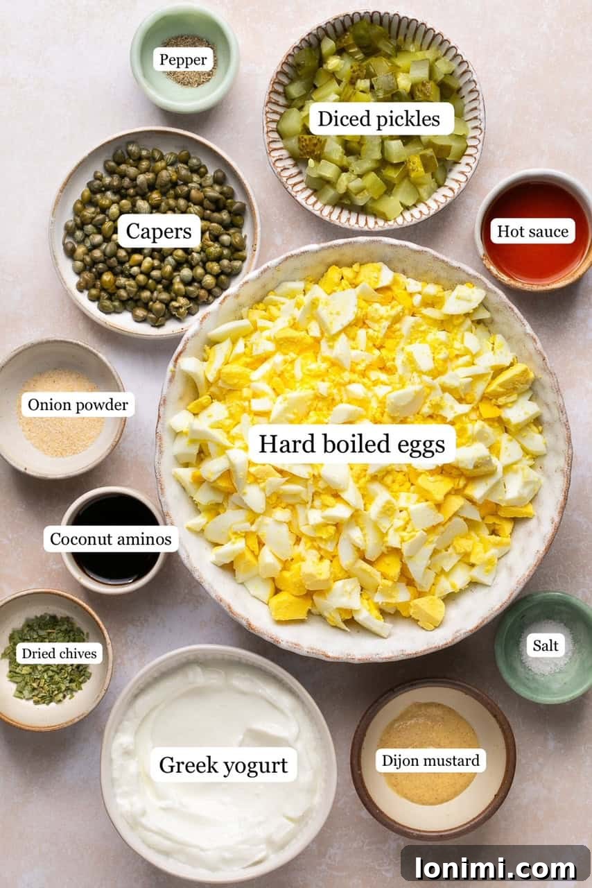 Recipe ingredients laid out in small, labeled bowls, showcasing fresh eggs, diced pickles, capers, and various seasonings.