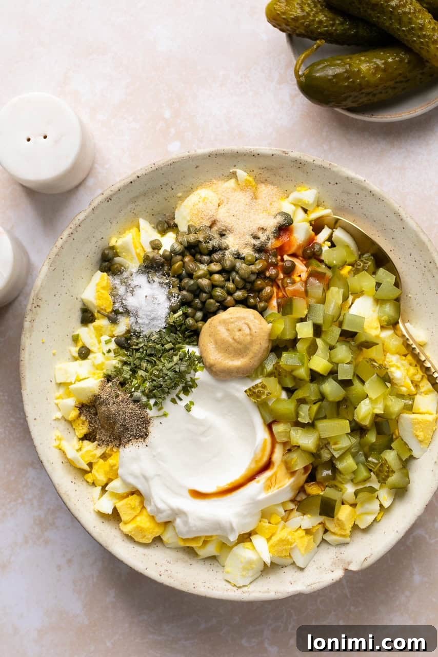 Recipe ingredients in a large mixing bowl before being combined, showing chopped eggs, pickles, and capers.