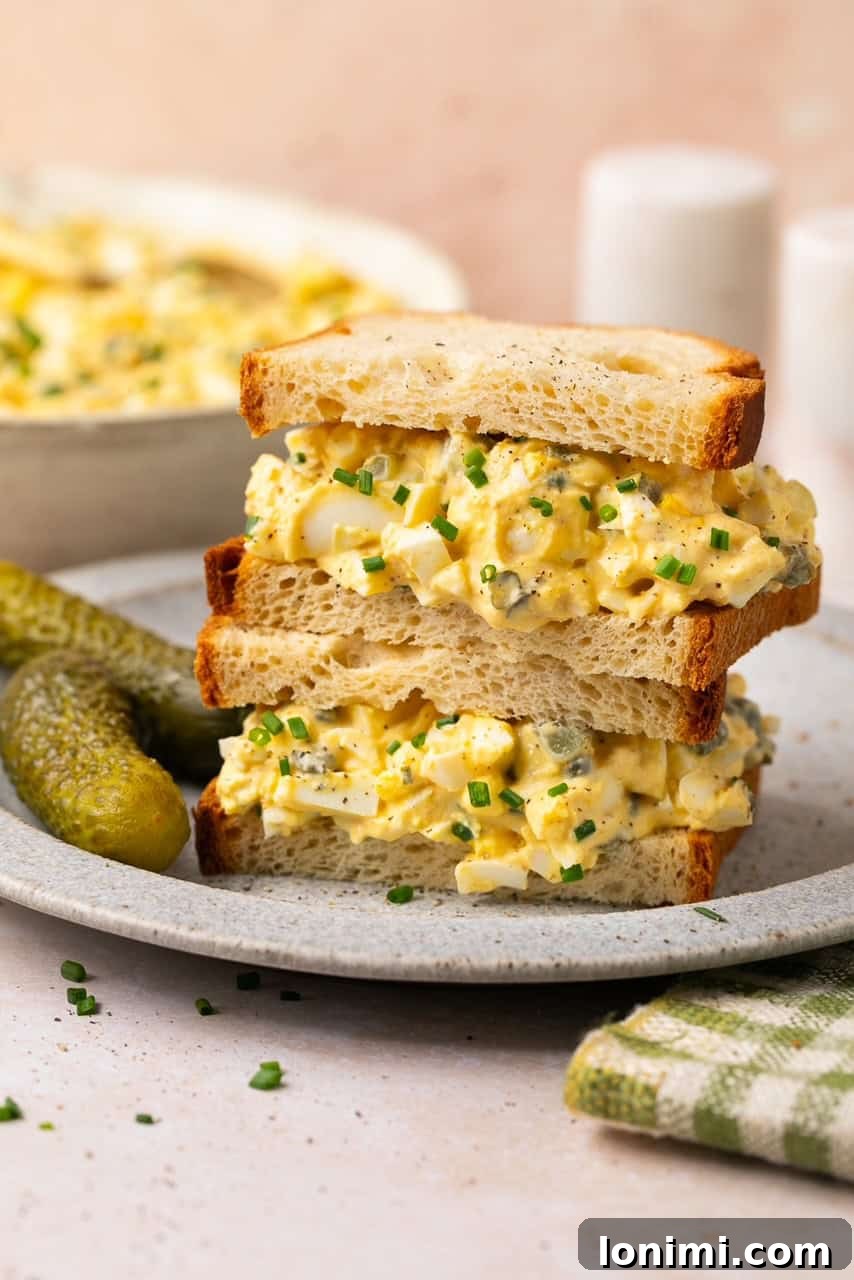 Two neatly stacked egg salad sandwiches on gluten-free bread, showing the creamy filling and a garnish of fresh dill.