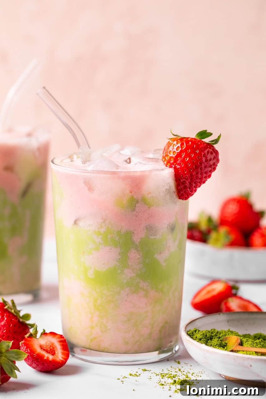 A close-up of the finished iced strawberry matcha latte with a straw and a fresh strawberry garnish, highlighting the texture of the cold foam.