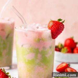 A vibrant iced strawberry matcha tea latte in a glass, with a fresh strawberry garnish, showcasing the beautiful green and pink layers.
