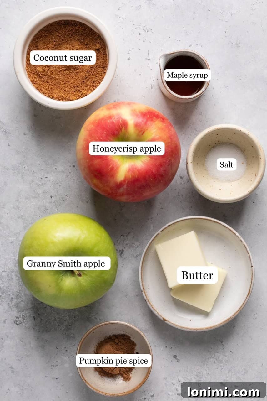Arrangement of fresh apples, coconut sugar, maple syrup, butter, pumpkin pie spice, and sea salt, showcasing all the ingredients needed for caramelized apples.