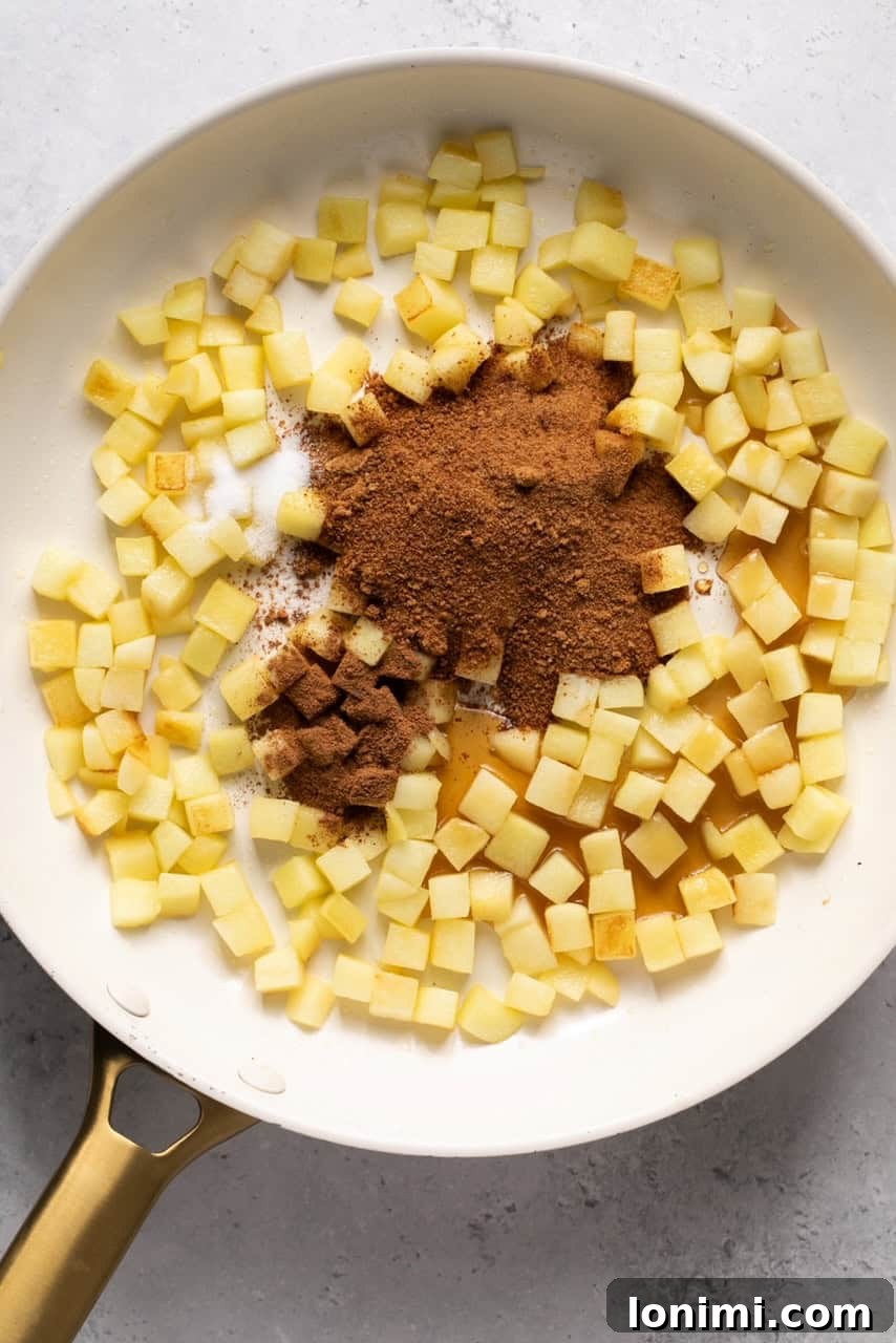 Spices, coconut sugar, and maple syrup added to the sautéed apples in a skillet.