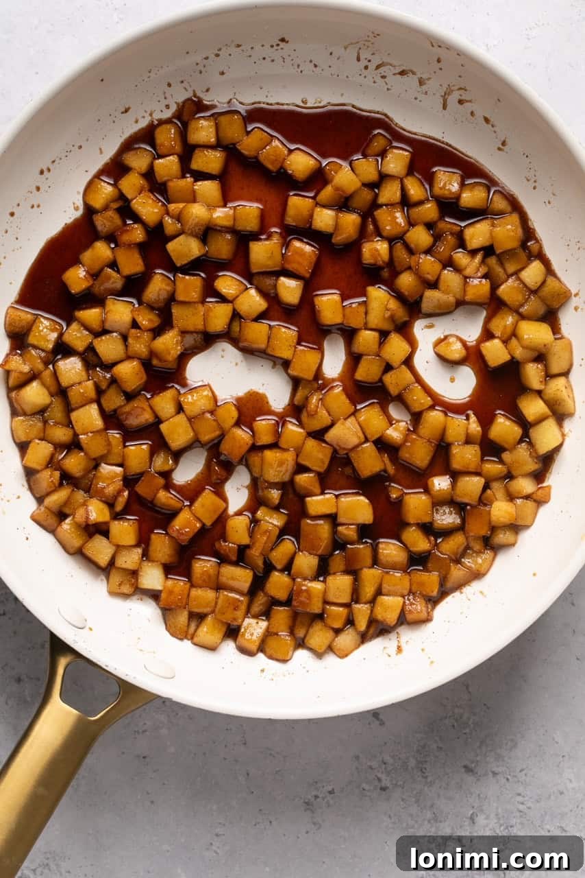 Apples stirring in a skillet, coated in a rich, bubbling caramelized sauce.