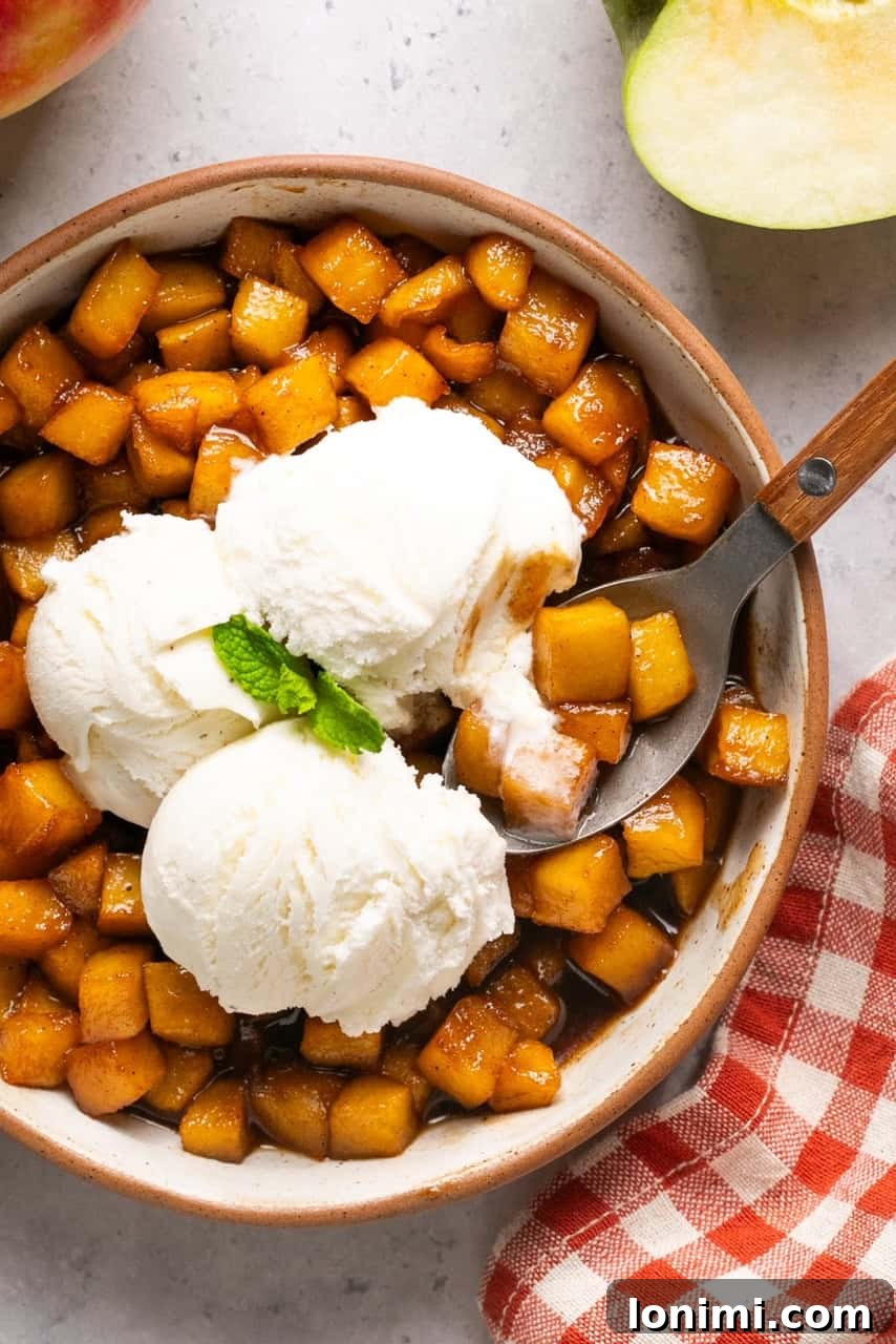 A spoon scooping a bite of caramelized apple and vanilla ice cream from a bowl, highlighting the dessert's deliciousness.