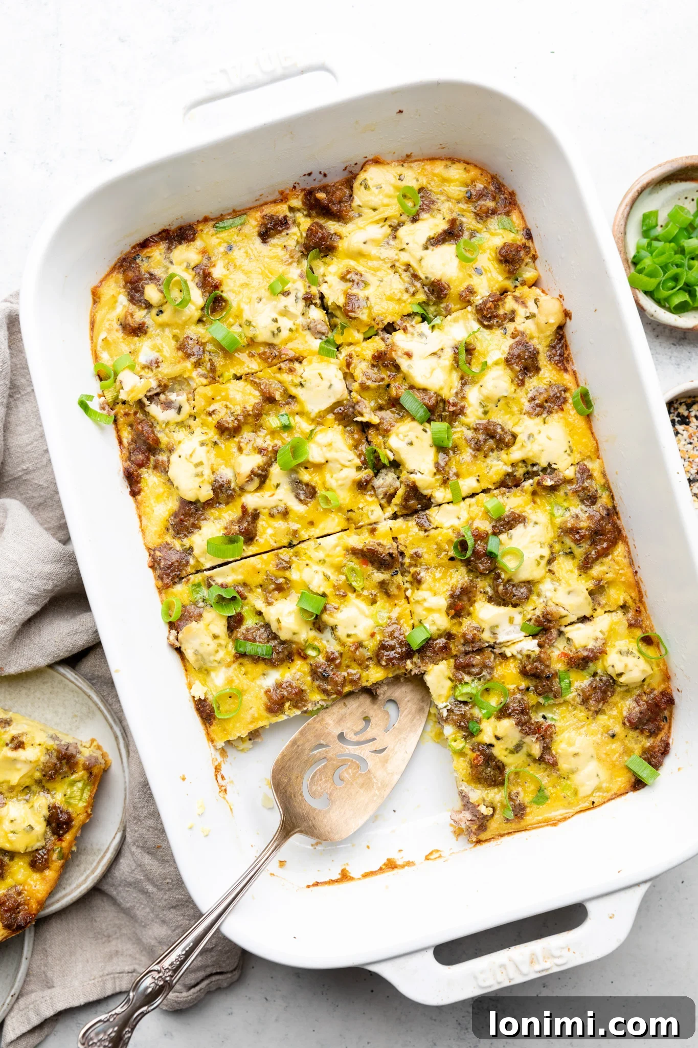 Gluten-free breakfast casserole topped with sliced green onions in a white Staub casserole dish on a light background.