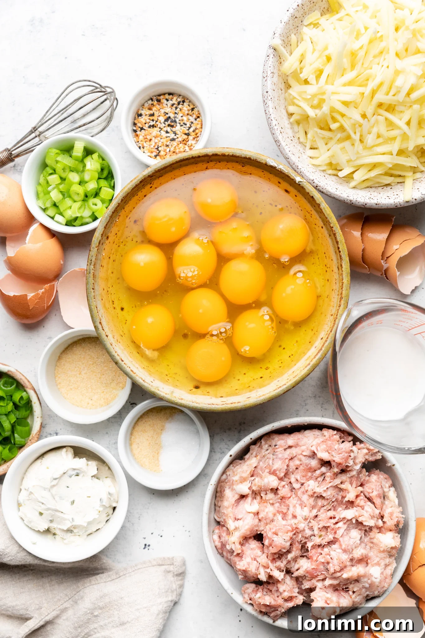 Ingredients laid out for paleo sausage hash brown breakfast casserole, including eggs, sausage, green onions, dairy-free cream cheese, and seasonings.