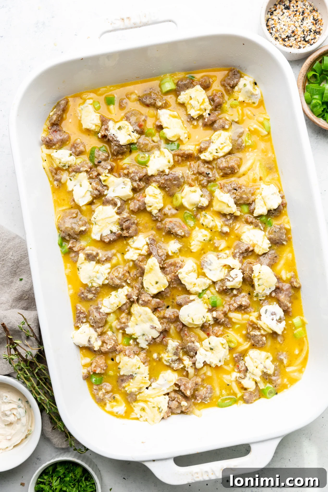 Egg mixture poured over hash browns, sausage, and green onions in a white casserole dish.