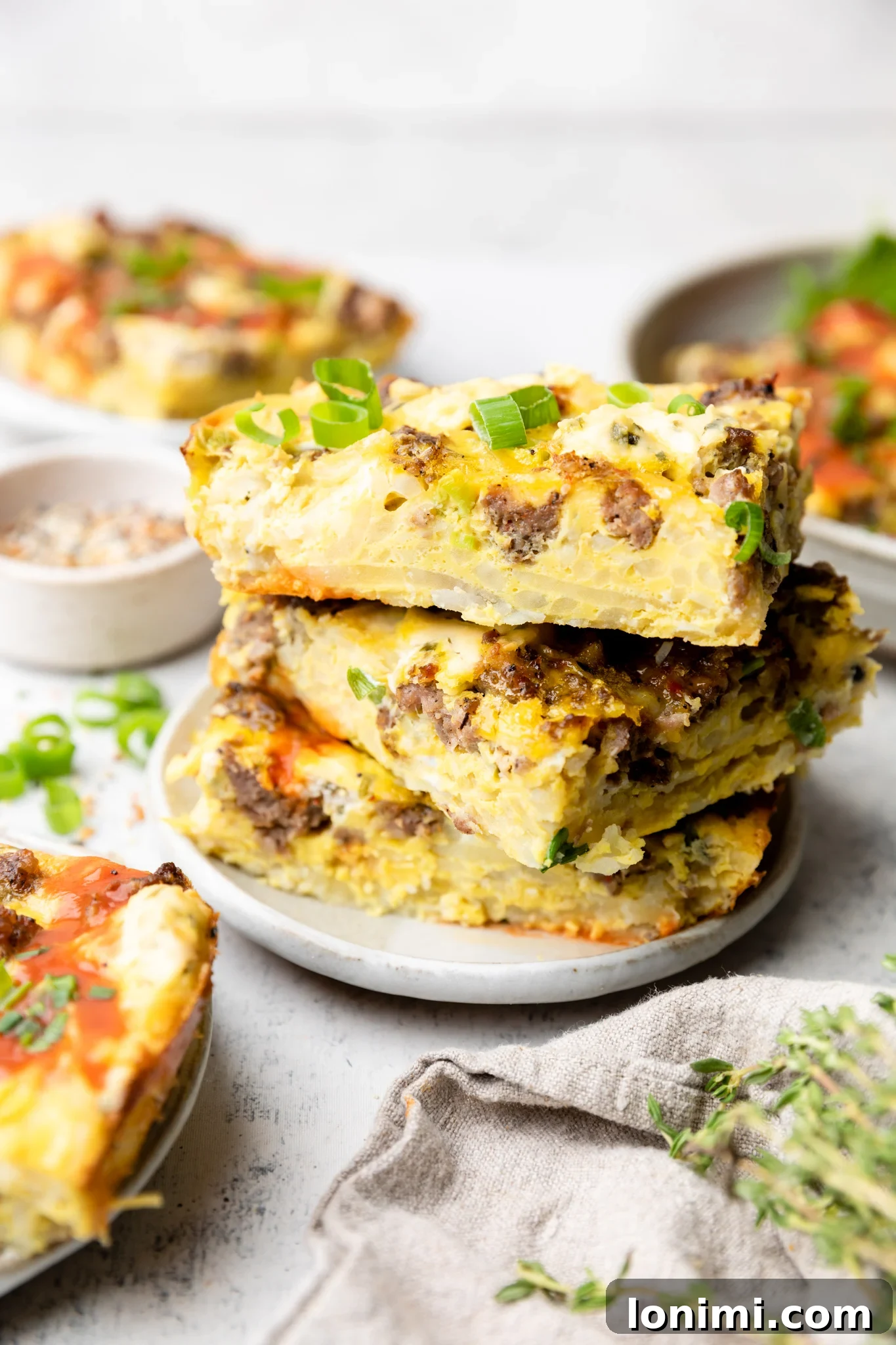 Square slices of sausage hash brown casserole stacked neatly on a plate, ready to serve.