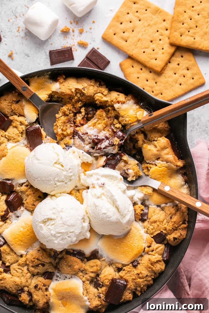 An overhead shot of a S'mores Chocolate and Marshmallow Cookie Skillet in a cast iron pan, topped with vanilla ice cream, ready to be served family-style.