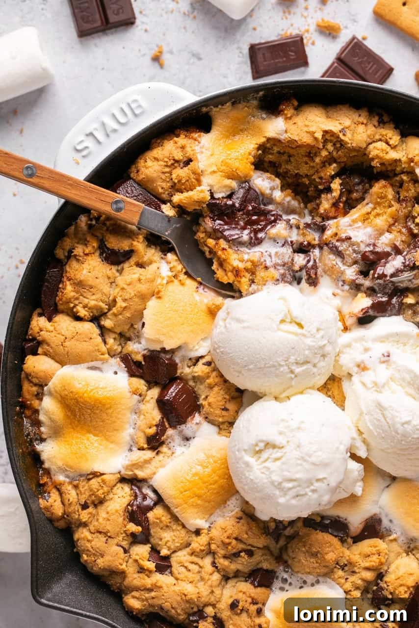 A spoon lifting a bite of the S'mores Chocolate and Marshmallow Cookie Skillet out of the pan, showing the gooey chocolate and melted marshmallow.