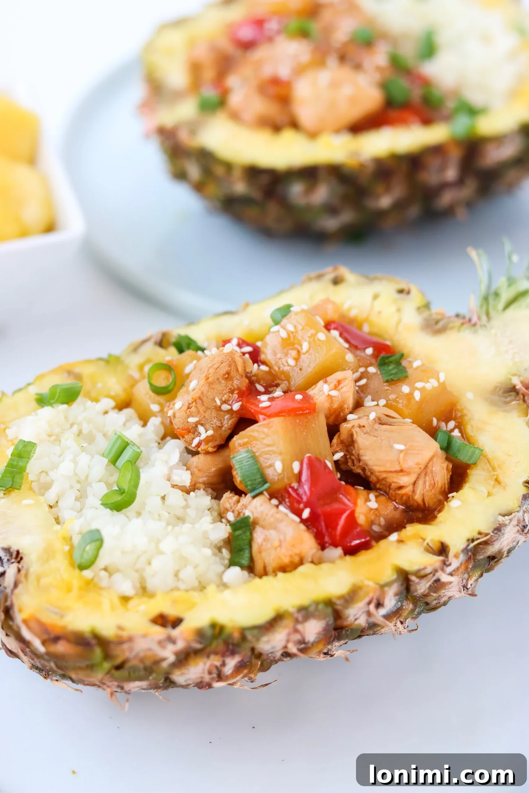 Delicious Whole30 Instant Pot Hawaiian Chicken served in a pineapple bowl, garnished with green onions and sesame seeds.