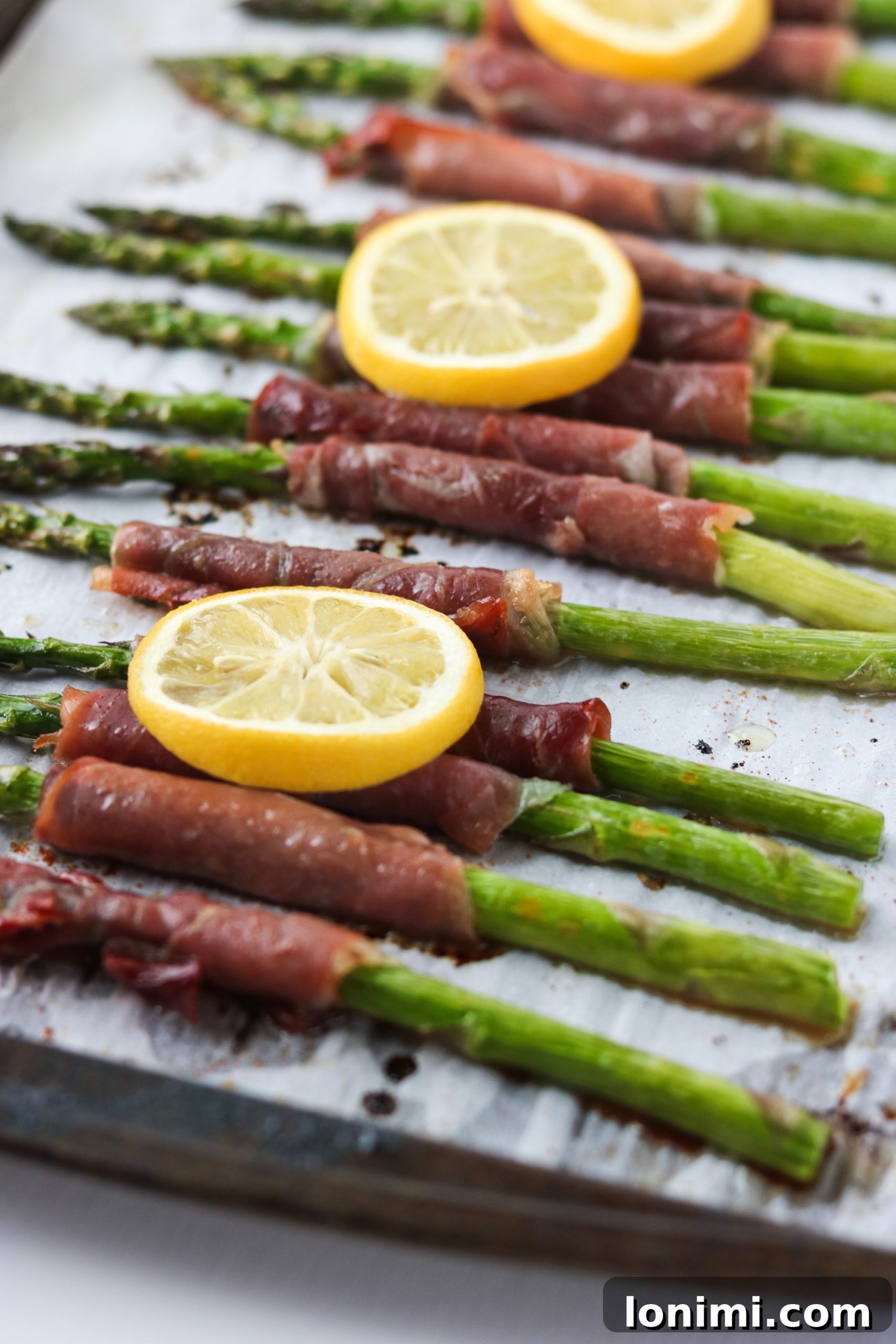 Freshly cooked lemony prosciutto-wrapped asparagus spears arranged on a baking sheet, ready to be served.