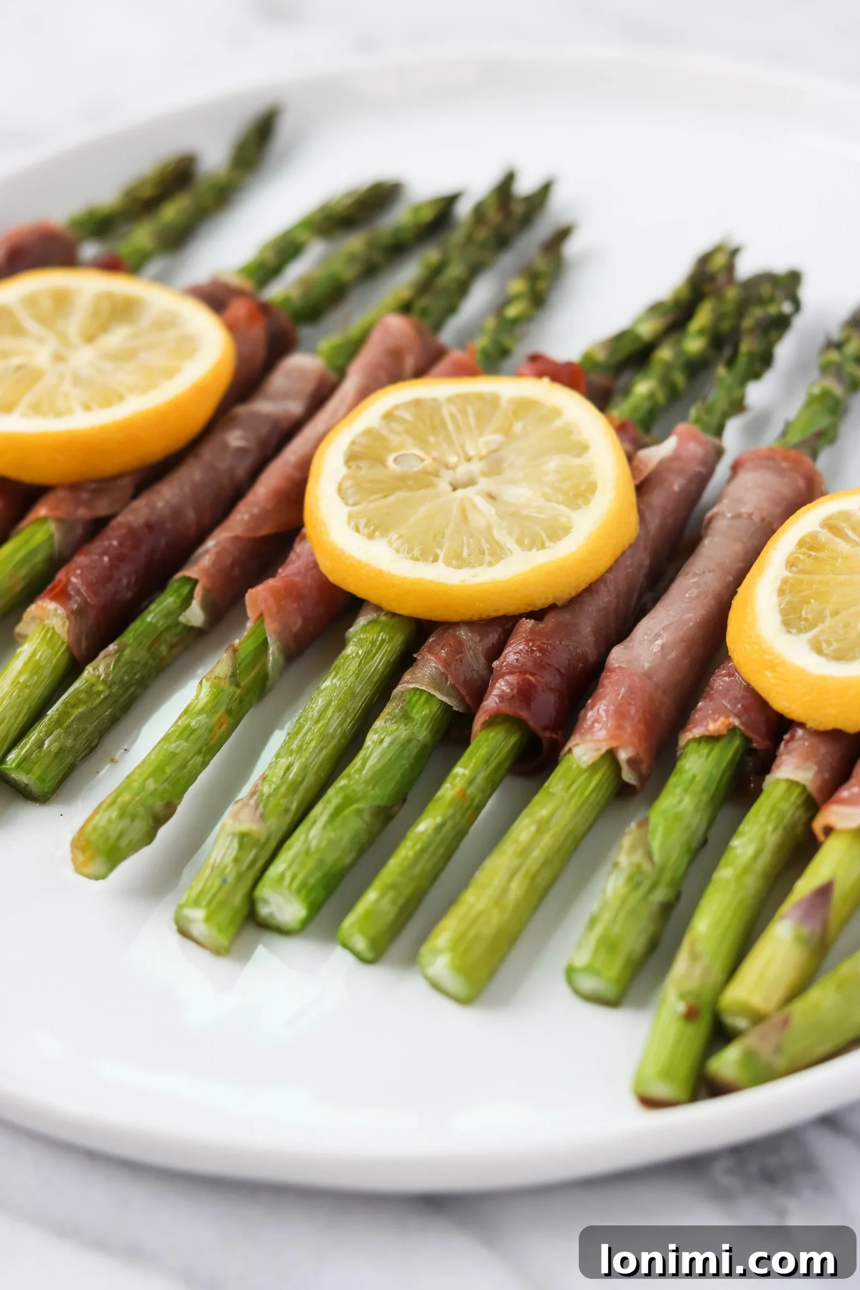 A serving of roasted lemony prosciutto-wrapped asparagus on a white plate, garnished with fresh lemon wedges, showcasing the delicious final dish.