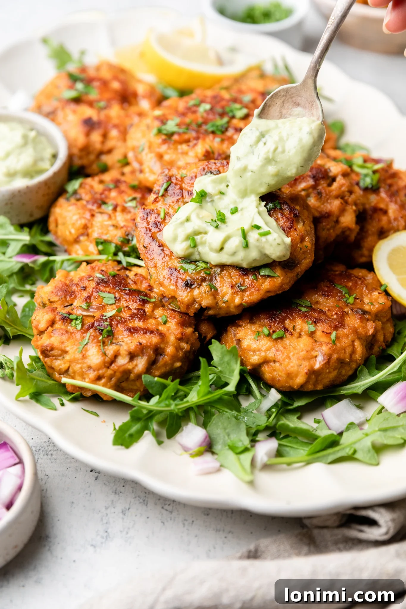 Spicy Southwest Keto Salmon Cakes with Creamy Avocado Aioli 2 Southwest salmon patties with avocado ranch aioli over greens on a white platter