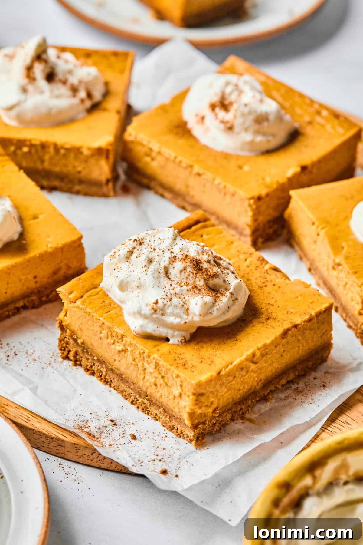 pumpkin cheesecake bars on parchment with whipped cream, garnished with pecans
