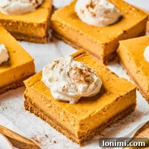 pumpkin cheesecake bars on parchment with whipped cream